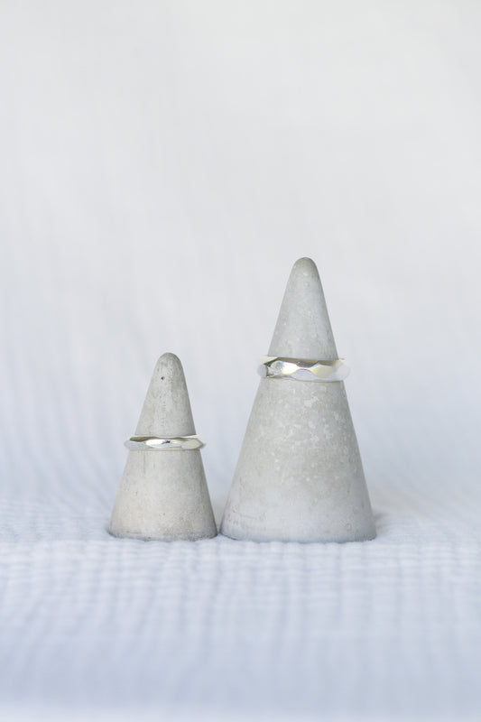 Two carved silver wedding rings on concrete stands, on a white background.