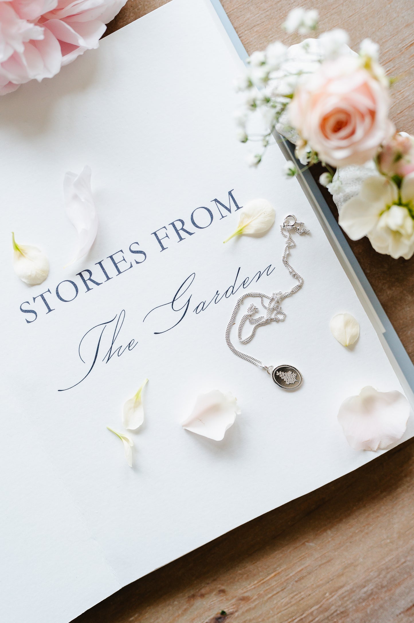 Dainty sterling silver necklace lying on an open book with some flowers.