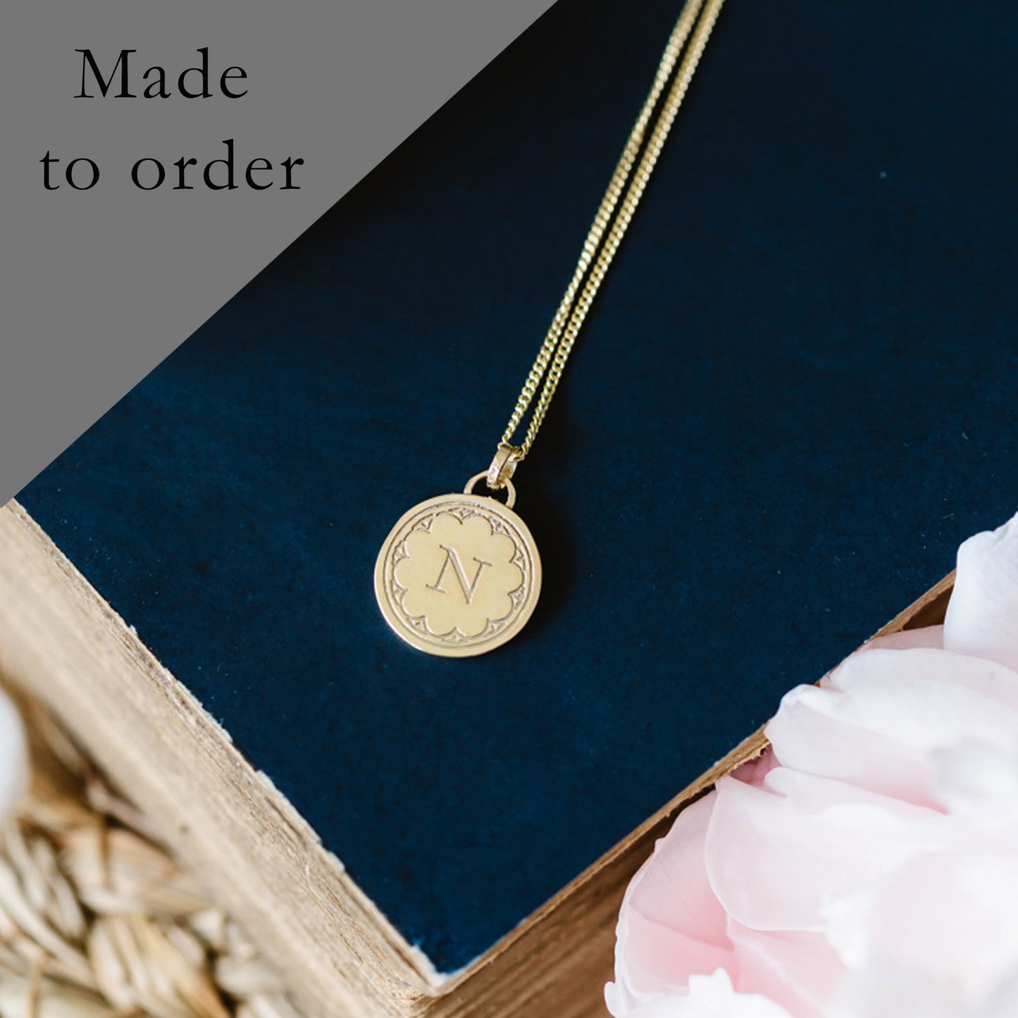 A solid 9ct yellow gold necklace with a round initial pendant, displayed on a book with a part of a golden chain visible.