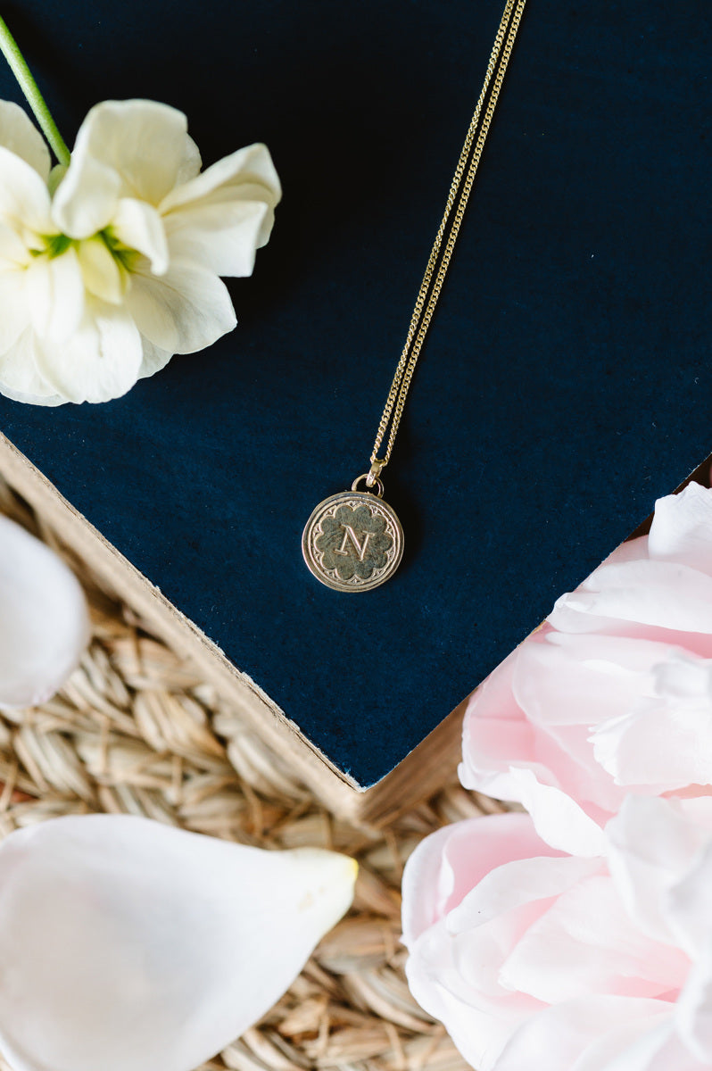 A dainty gold initial necklace sitting on a book with flowers