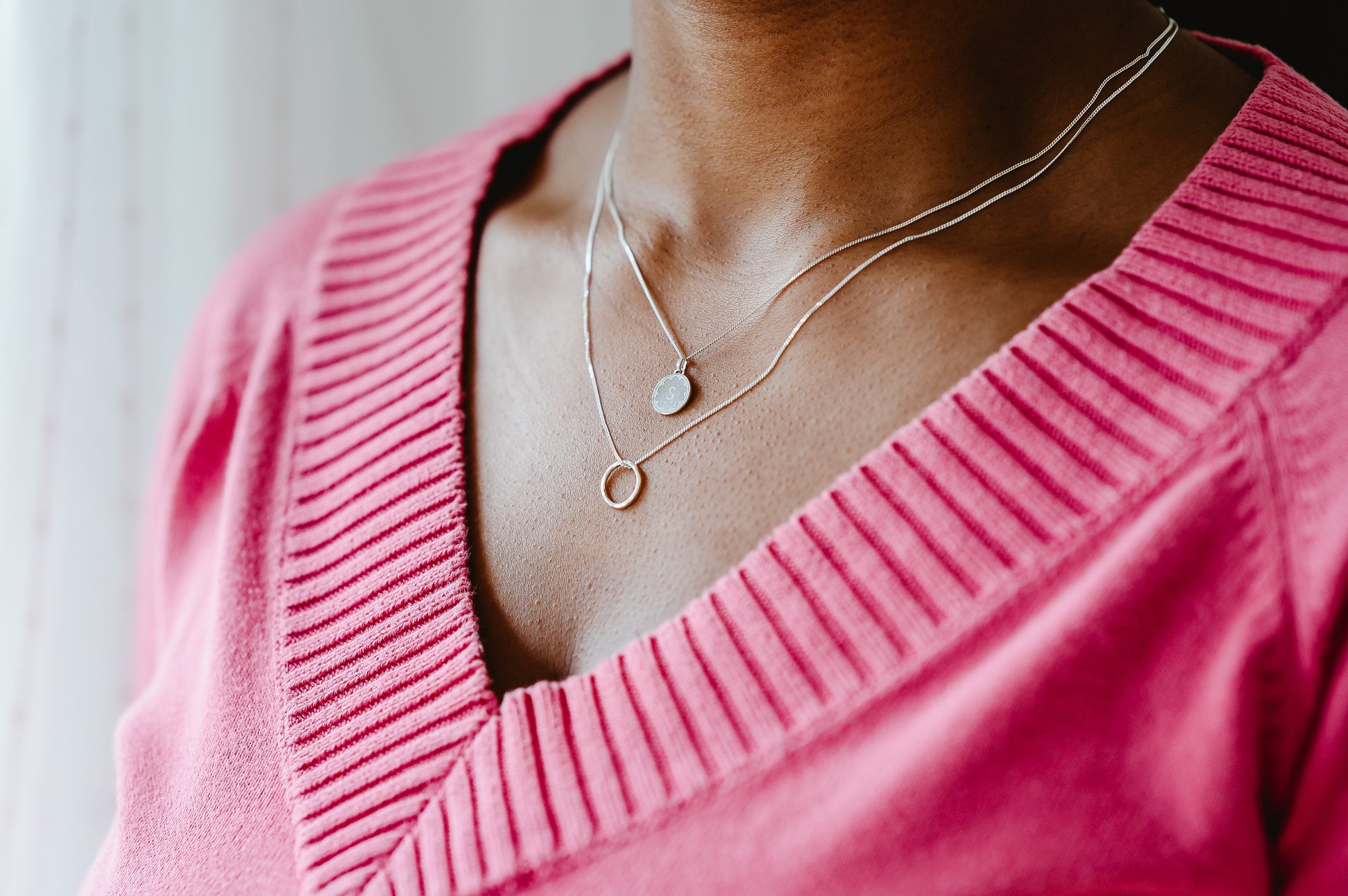 A round initial necklace in sterling silver being worn with a silver oval.