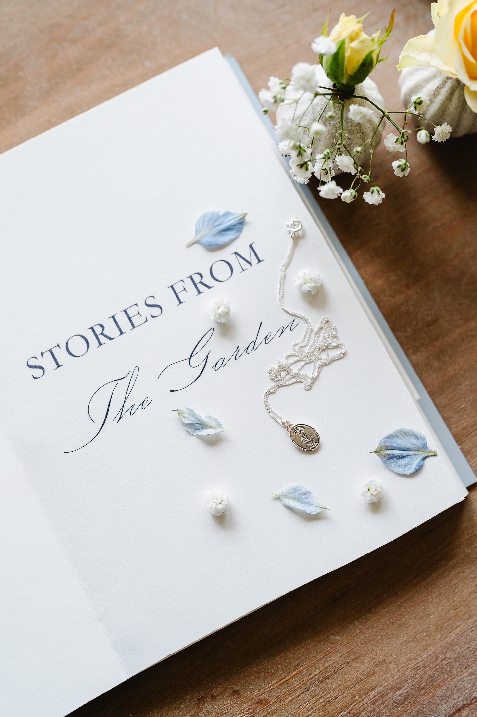 necklace with a carnation flower in solid sterling silver. Necklace shown lying on a book with some flowers