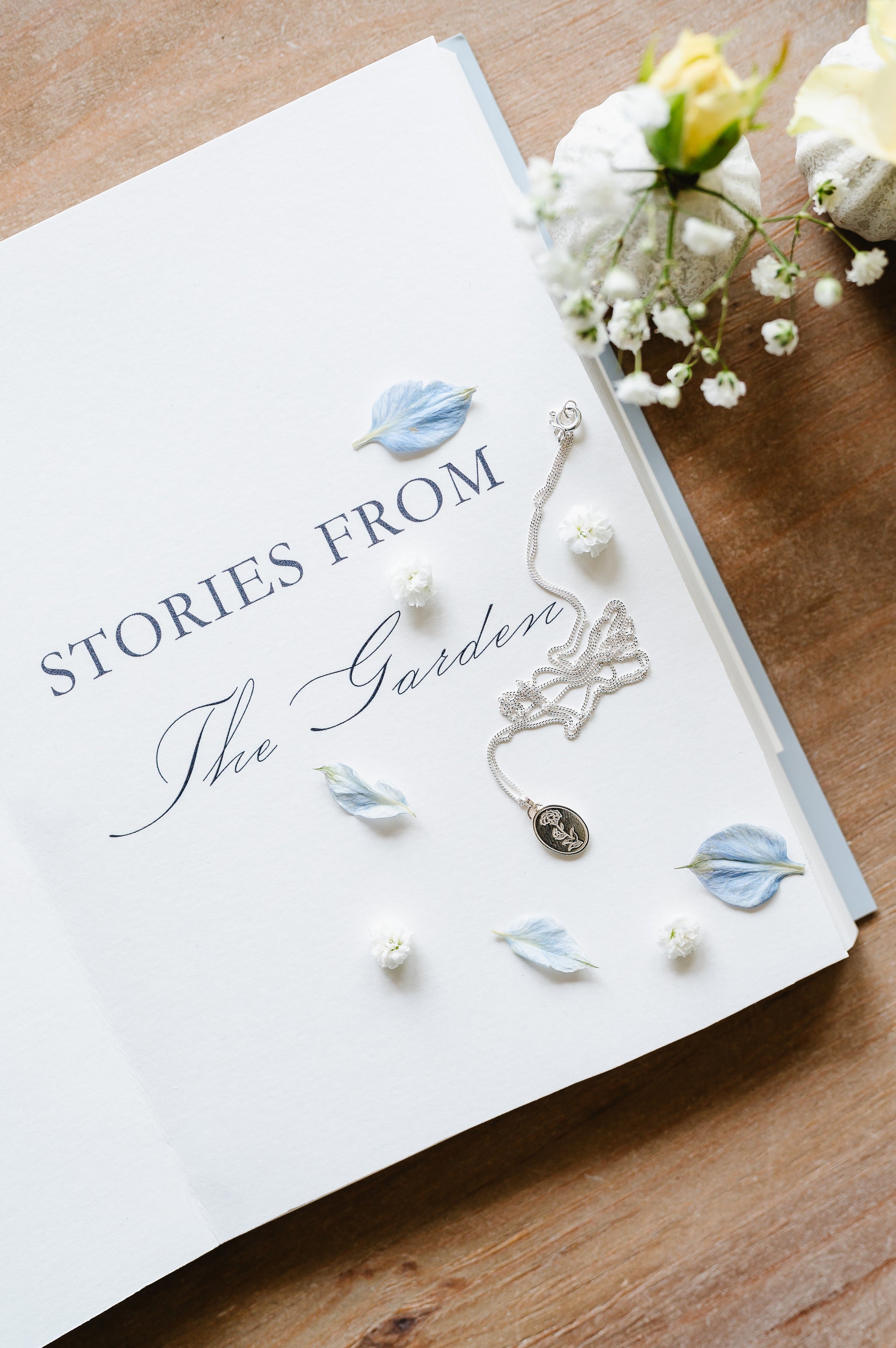 a sterling silver necklace with a carnation lying on a book with flowers