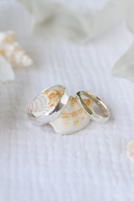 Carved silver wedding rings leaning on seashells.