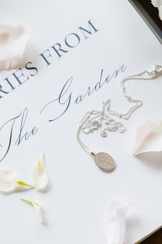 A stering silver necklace with a sweet pea flower. Oval coin necklace with a dainty sweet pea flower image.