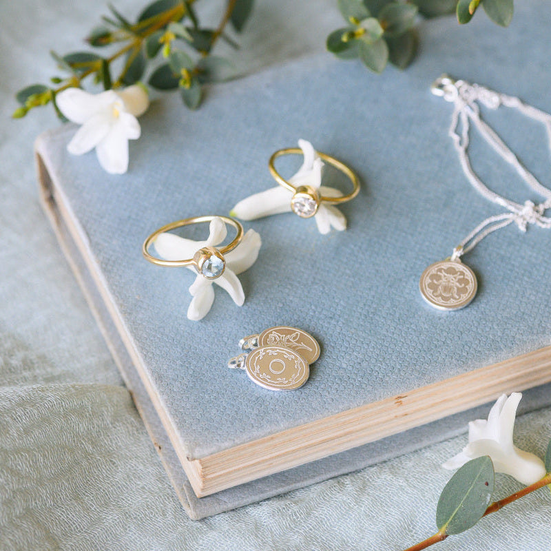 A pair of solitaire rings sitting on a book, with some engraved charms.