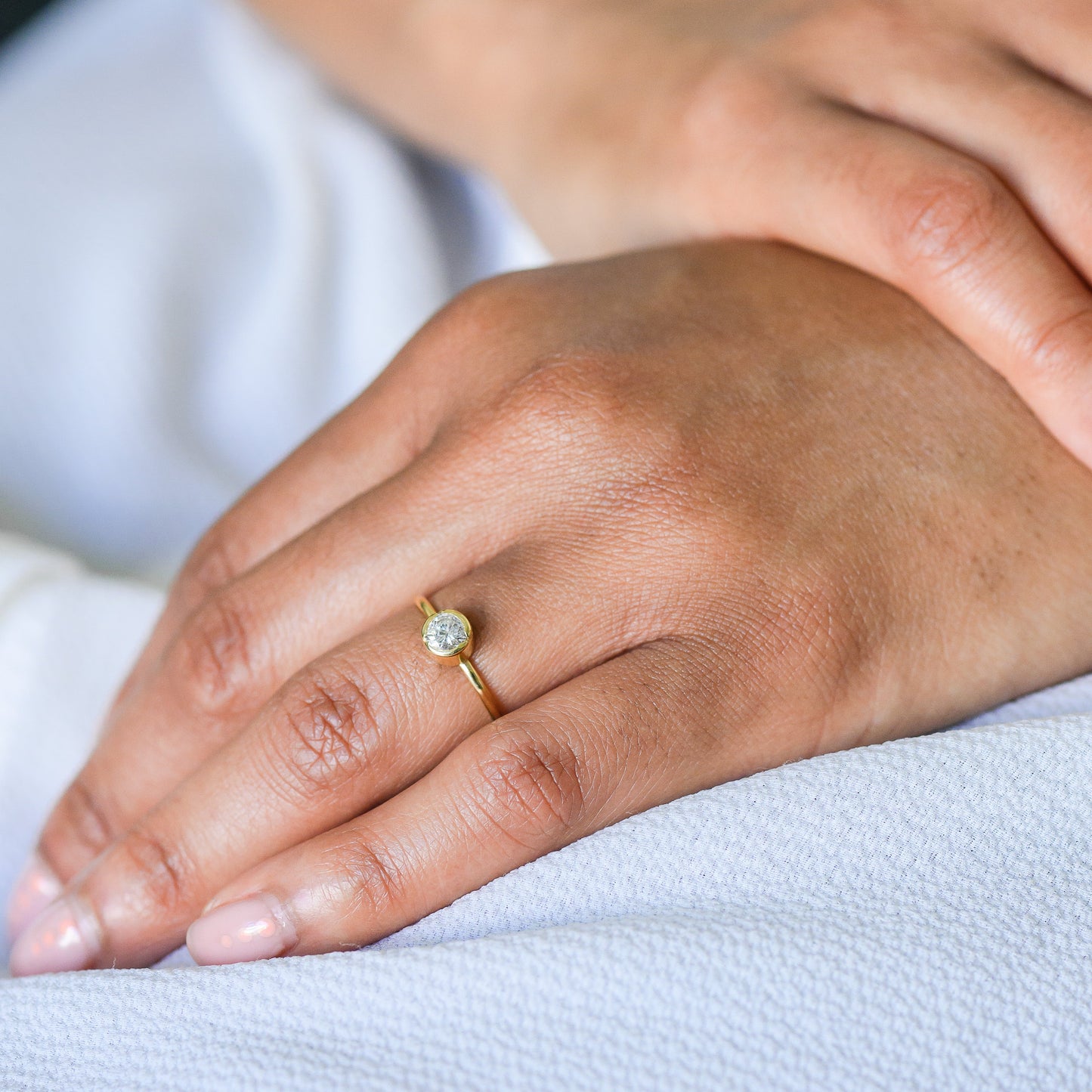 Close-up of a hand wearing a gold solitaire ring with a diamond on a light background