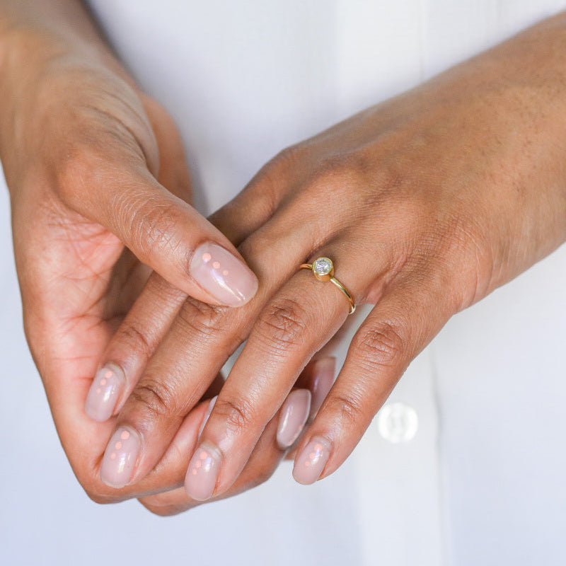 Two hands with a gold and diamond solitaire ring on a white background