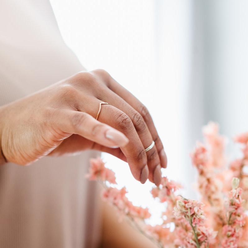 A hand wearing a slim wishbone in rose gold, and a pair of silver midi rings.