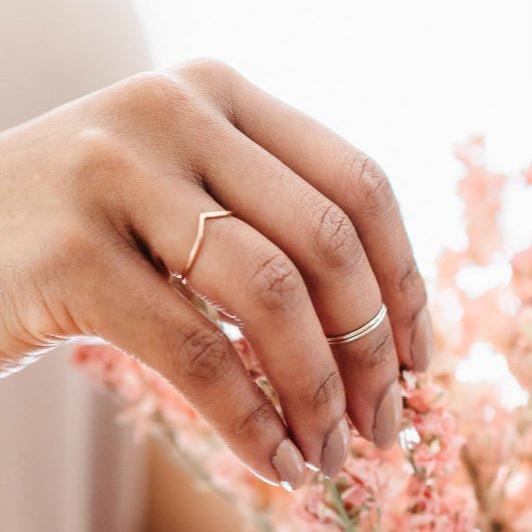 A hand wearing a thin rose gold wishbone and a pair of silver mid rings.