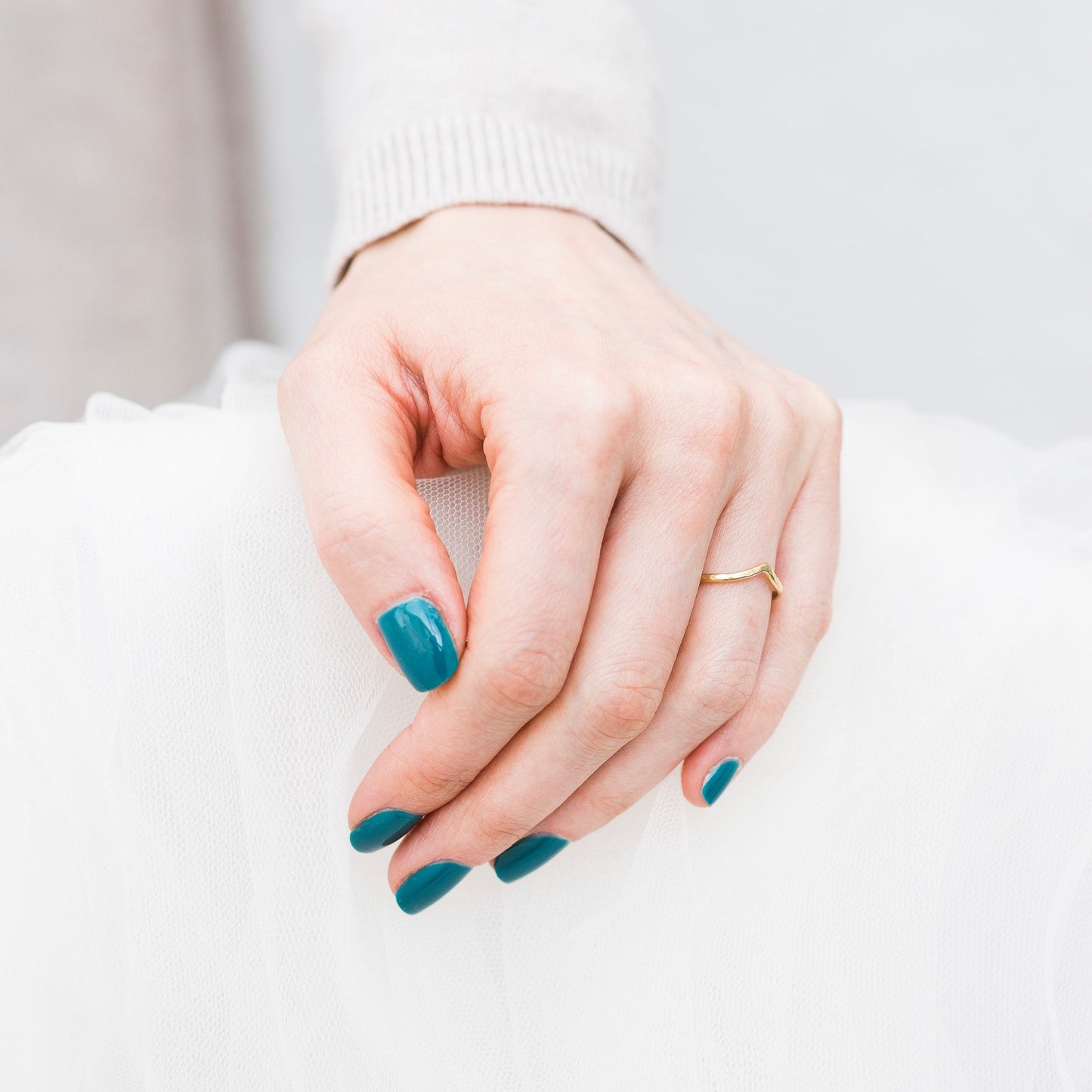 18ct yellow gold wishbone ring, worn on a hand with blue nail polish