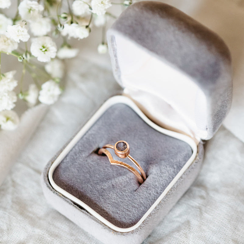 Rose gold ring in an open gray velvet box with white flowers in the background