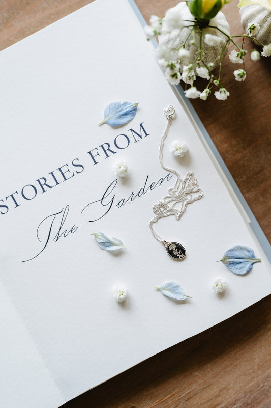 A dainty sterling silver necklace with a carnation flower, lying on an open book.