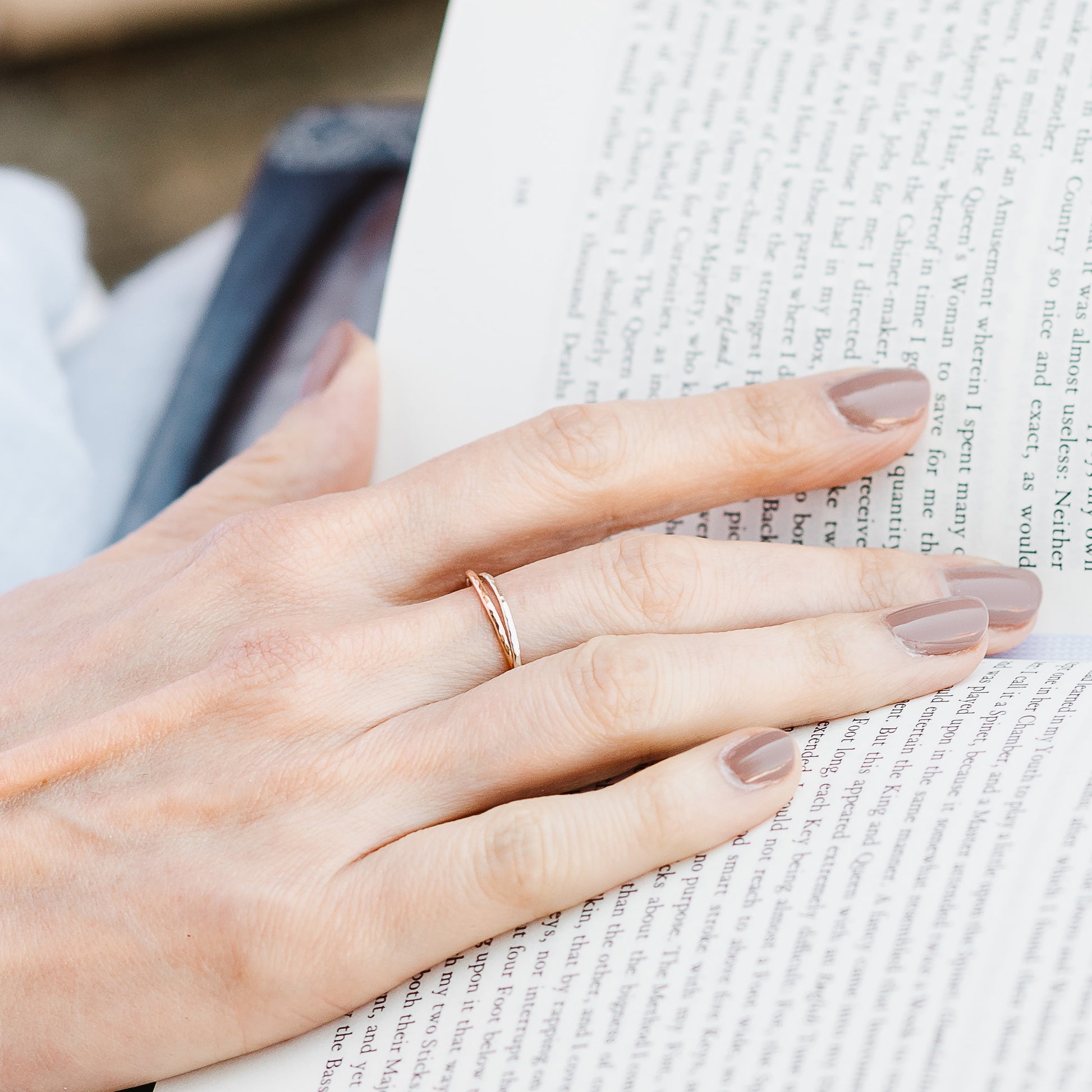 A pair of joined or russian wedding ring style bands in 9ct white and rose gold, with a hammered finish, hand resting on an open book