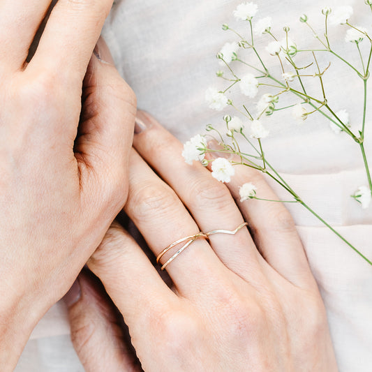 a pair of joined bands in 9ct white and rose gold, hammered finish and a 1.2mm wishbone in 9ct white gold with hammered finish being worn, on a pale background with some gyp