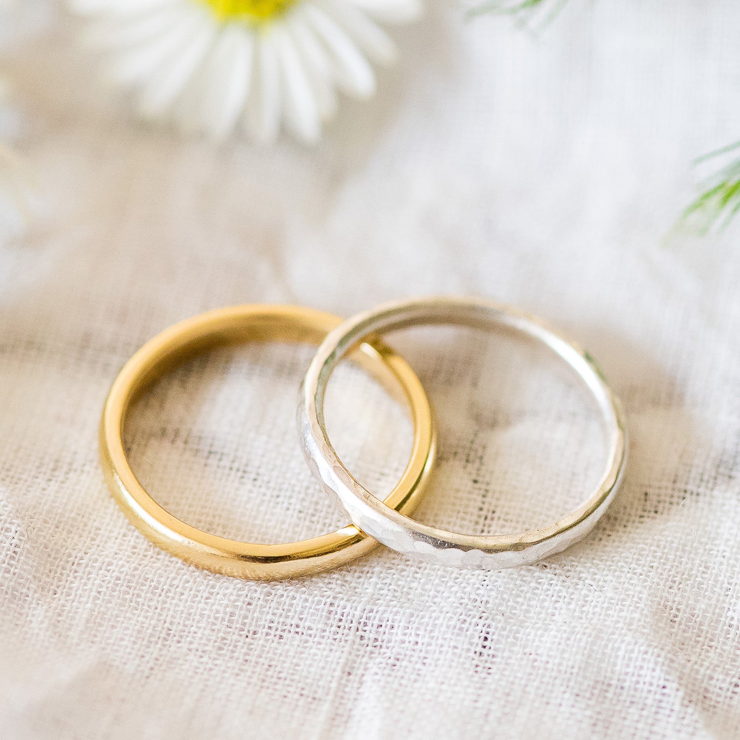 A pair of 2.3mm D shaped band, one 18ct yellow gold, one sterling silver hammered, close up on fabric background