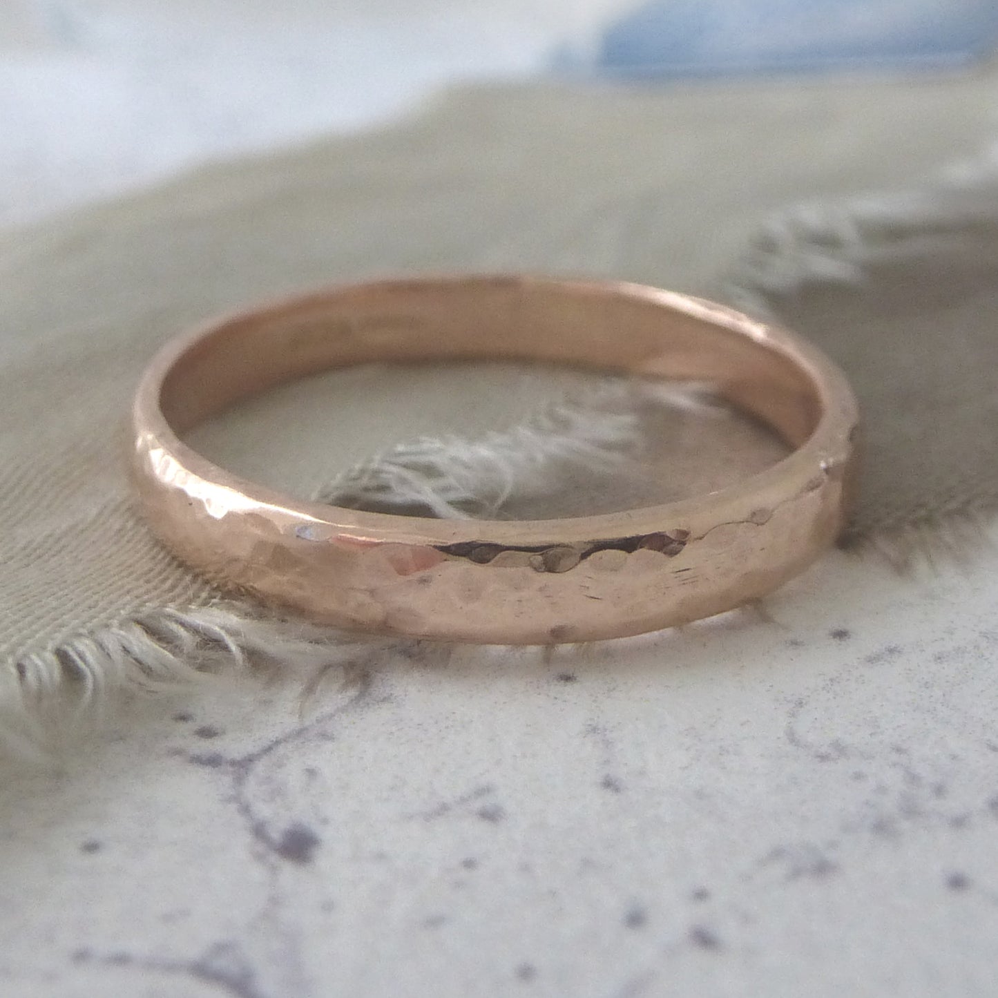 9ct rose gold wedding ring with hammered finish, close up on ribbon and paper background