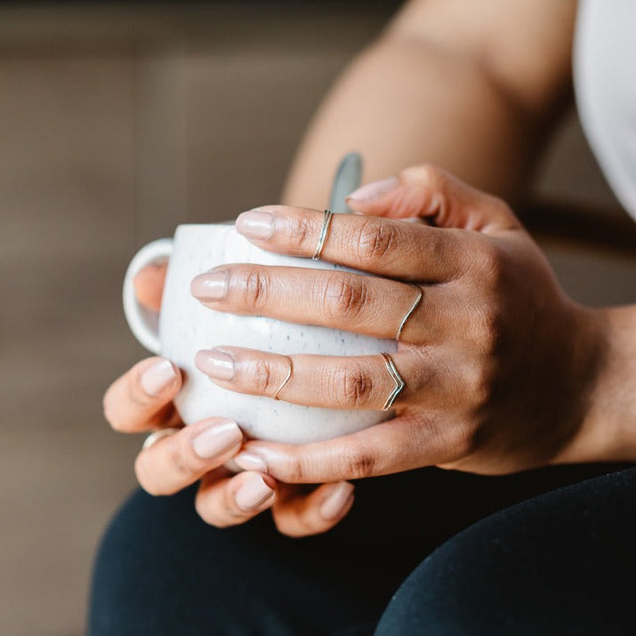 A hand wearing a selection of thin rings, holding a mug