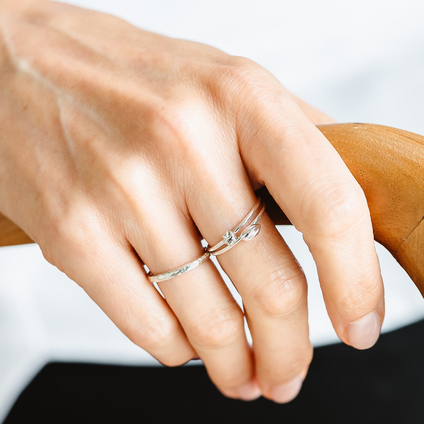 A hand wearing a hammered band in silver, and a set of 2 rings in recycled silver