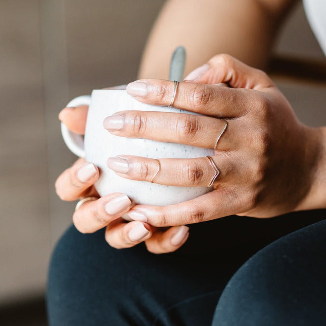 A selection of thin rings in sterling silver and 9ct gold, hand holding a mug