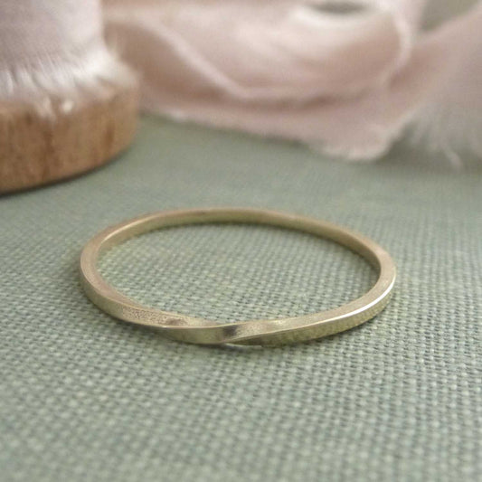 A thin 9ct gold ring with a twist, lying on a textured book cover.