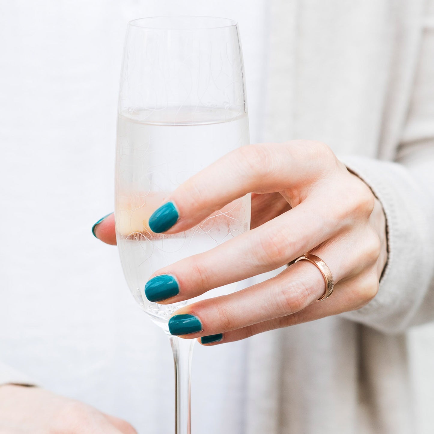 recycled 9ct rose gold wedding band, being worn on a hand with blue nails holding a champagne flute