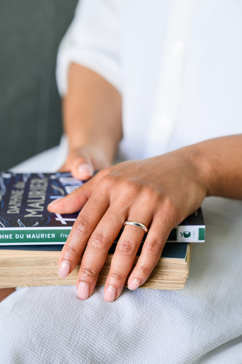 Person holding a stack of books with a carved wedding ring on their finger