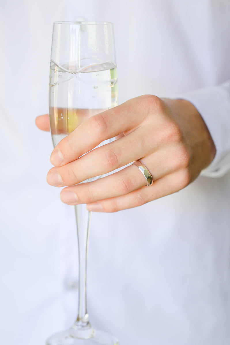 Sterling Silver Wedding Ring with carved detail, being worn by a hand holding a champagne flute