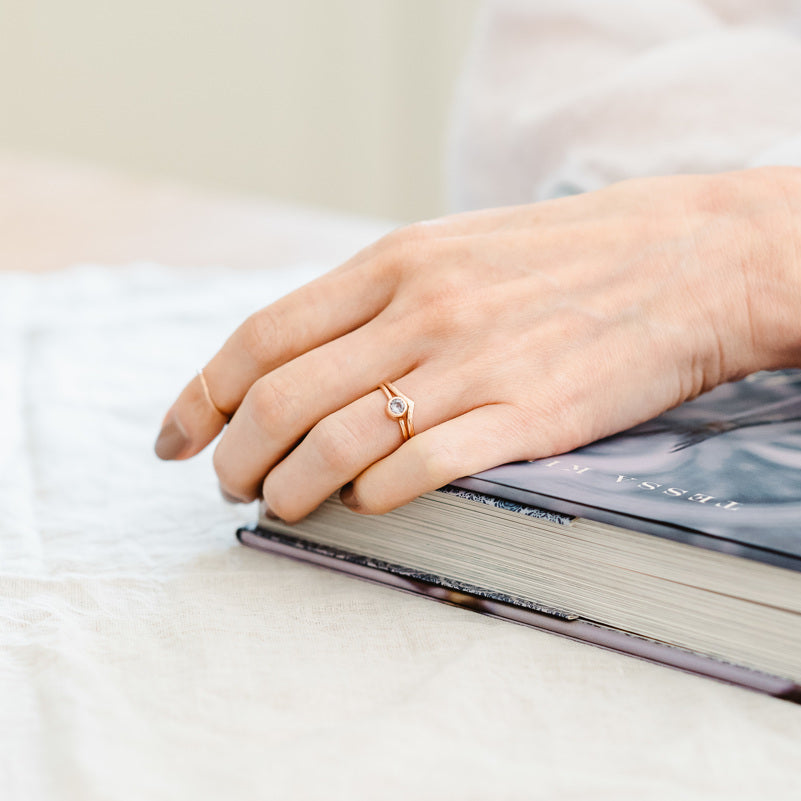 9ct rose gold wishbone ring. Shown worn by a hand leaning on a book.