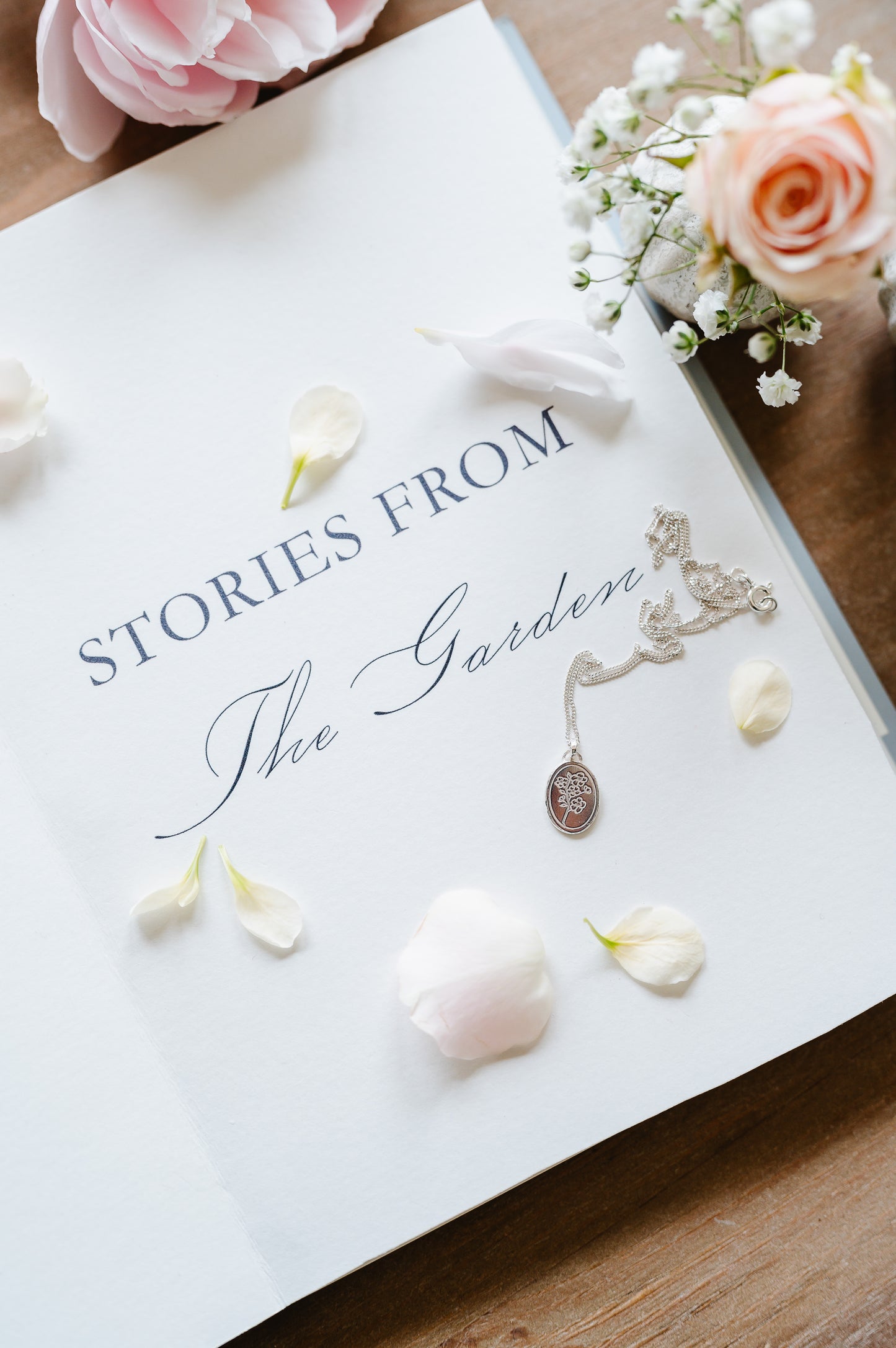 A cherry blossom necklace in sterling silver, lying on a book with flowers in the background.