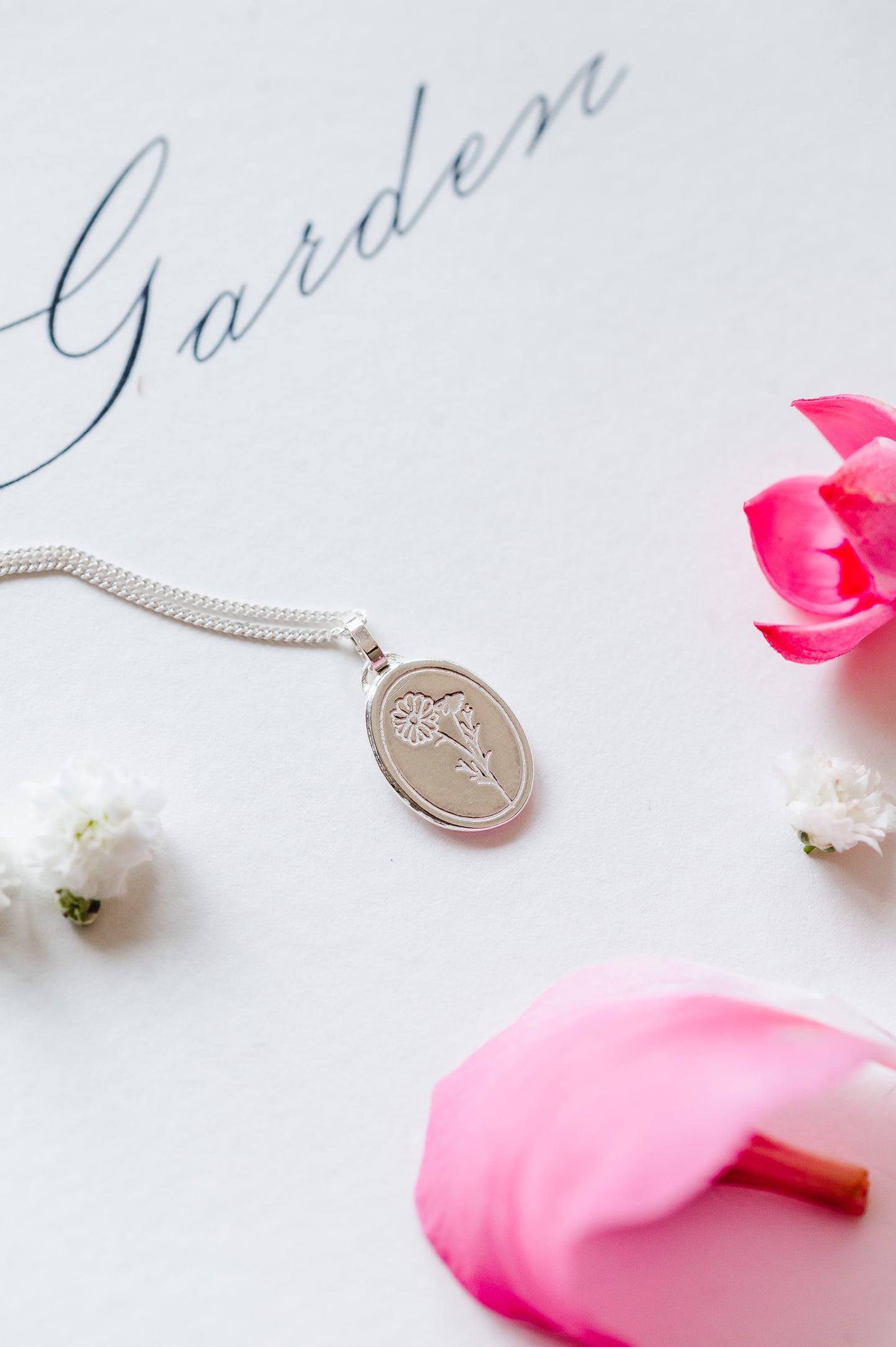 A sterling silver necklace with a cosmos flower on a white background. 