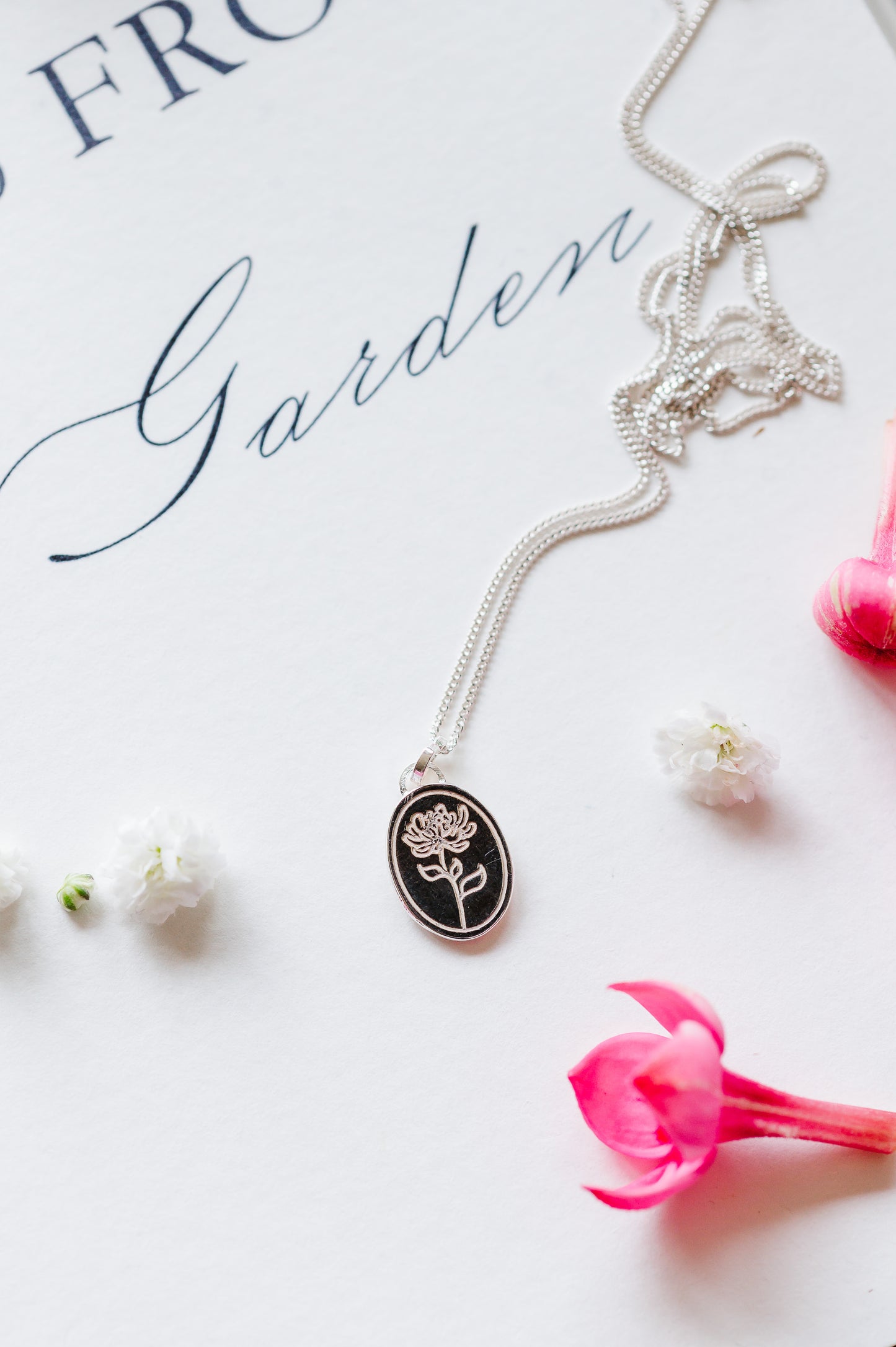A dainty flower necklace in sterling silver, with a chrysanthemum, lying on a white page with some buds.