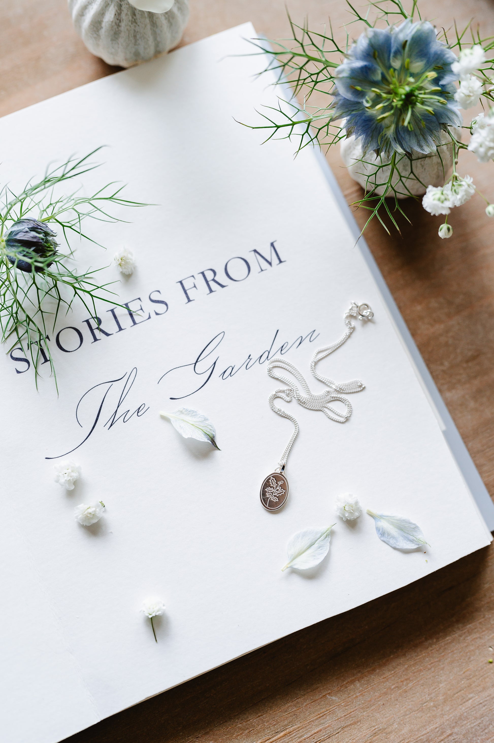 A dainty sterling silver necklace with a holly sprig lying on a book. 
