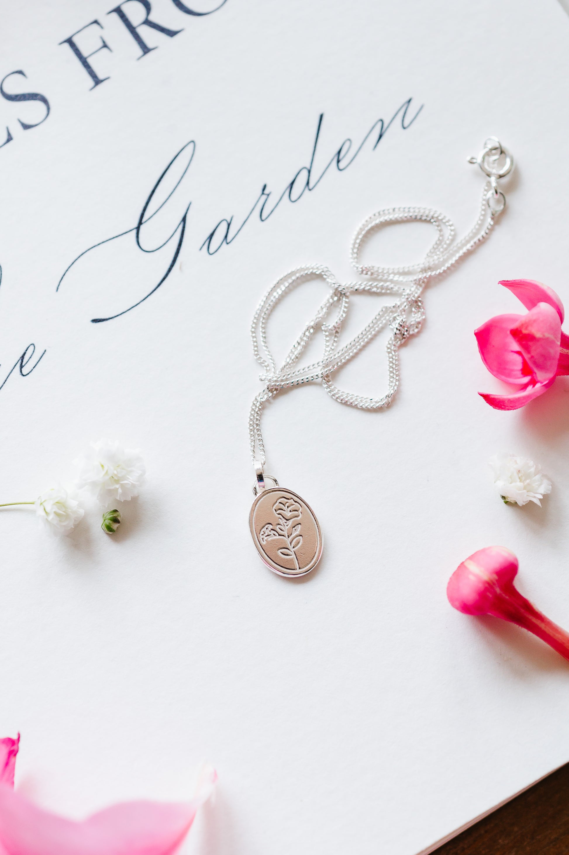 A sterling silver necklace with a morning glory flower lying on a white background with some flowers. 
