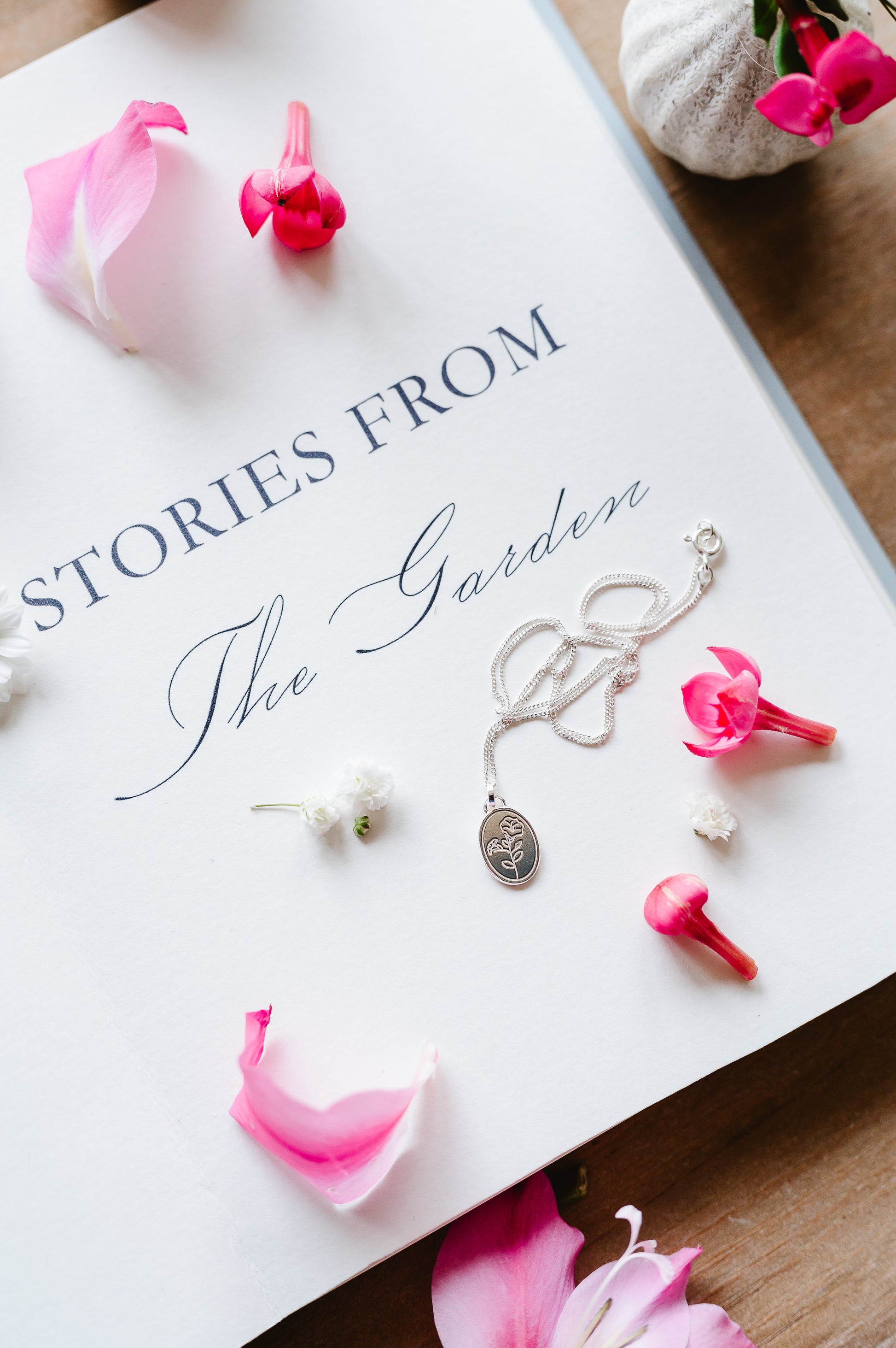 A dainty sterling silver necklace with a morning glory flower lying on an open book. Scattered petals on the page.