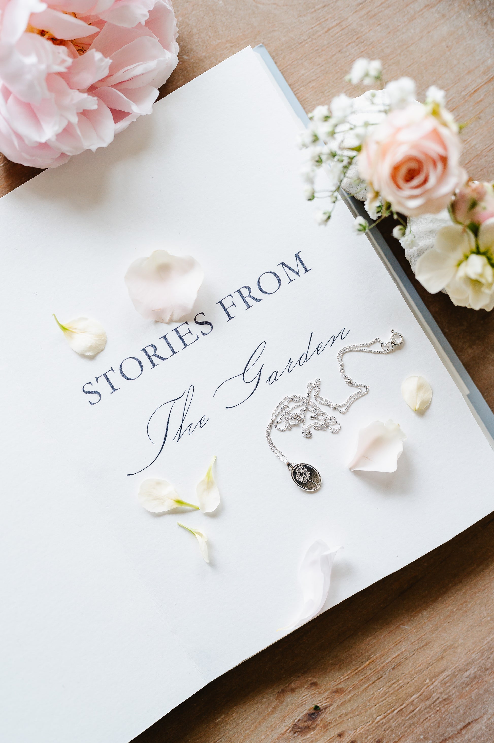 Dainty necklace in sterling silver with a sweet pea flower, lying on a book with some flowers.