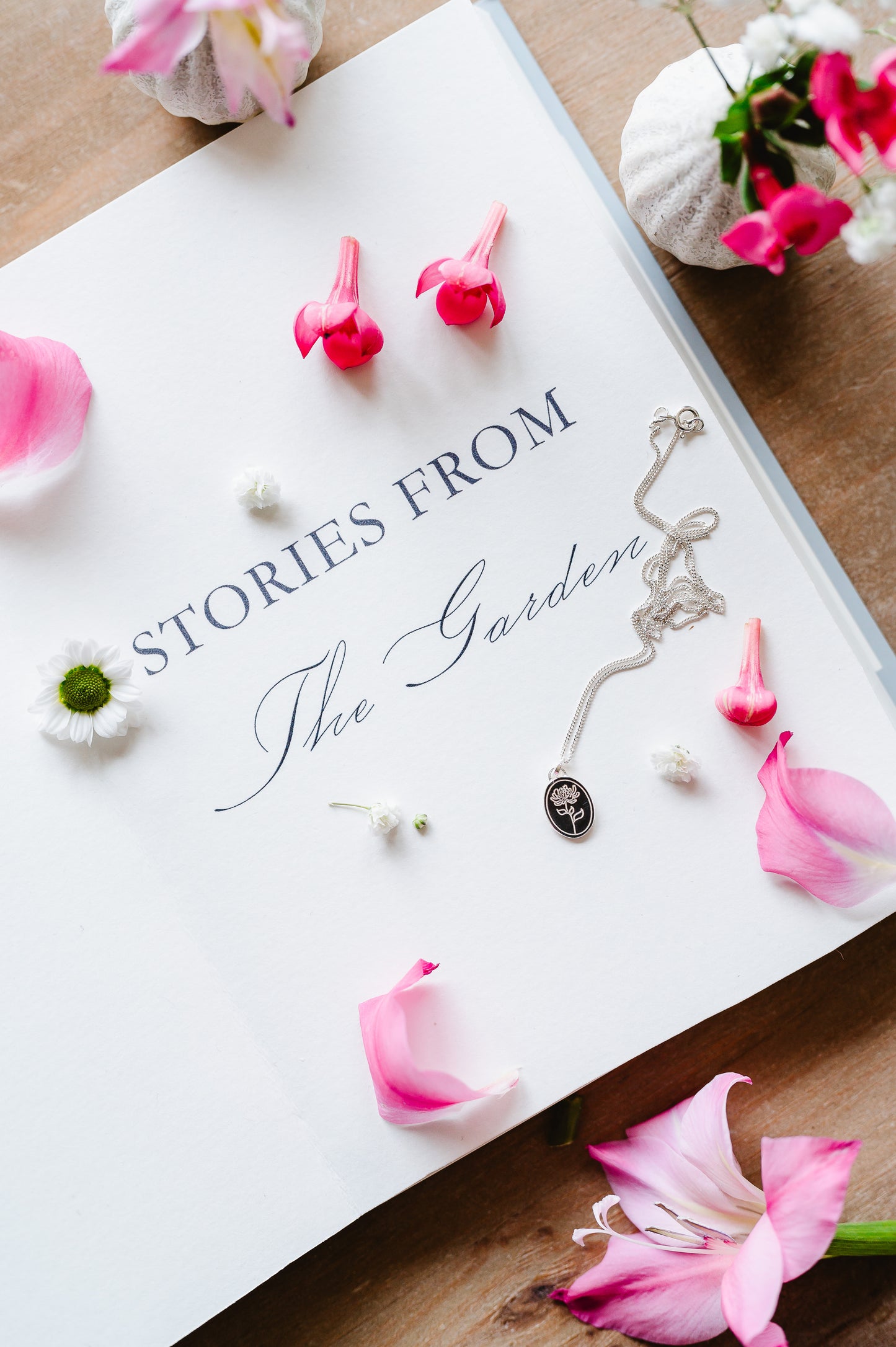 A dainty flower necklace in sterling silver with a chrysanthemum flower. The silver necklace is lying on a book with flowers in the background.