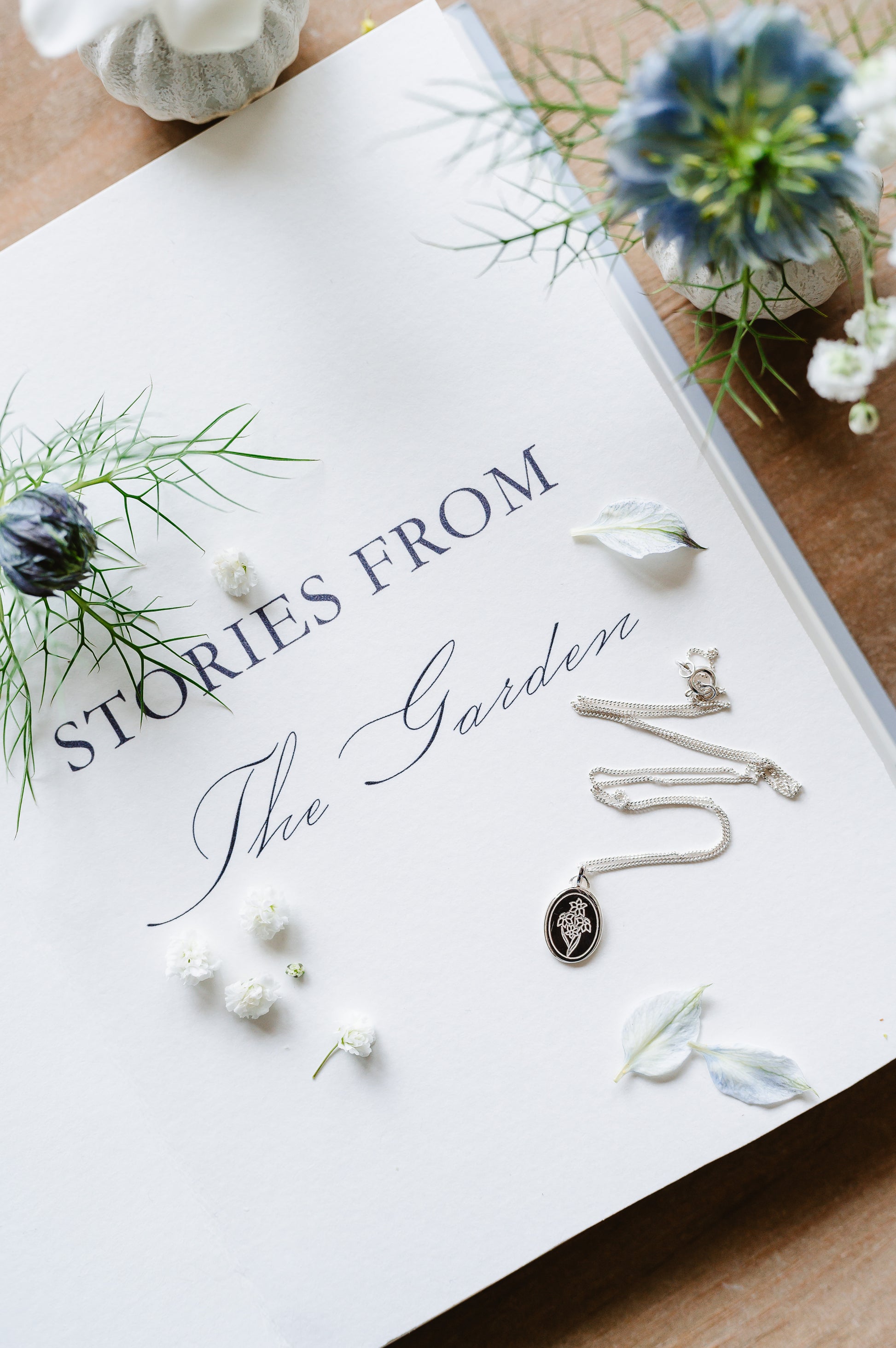 A flower necklace with a bunch of narcissus in sterling silver. The necklace is lying on a book page with flowers in the background.