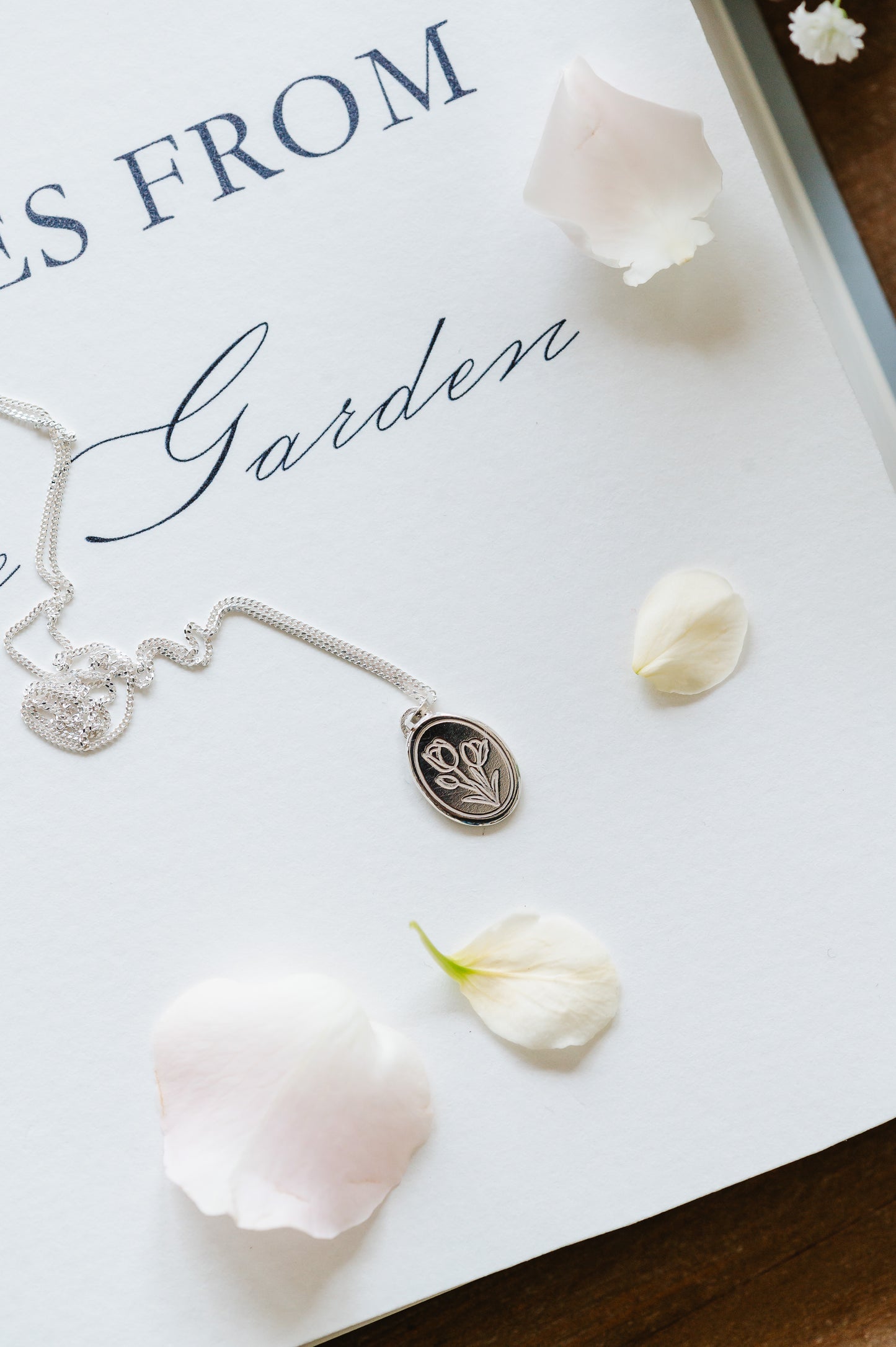 A dainty flower necklace with a tulip in sterling silver, lying on a page with some petals. 