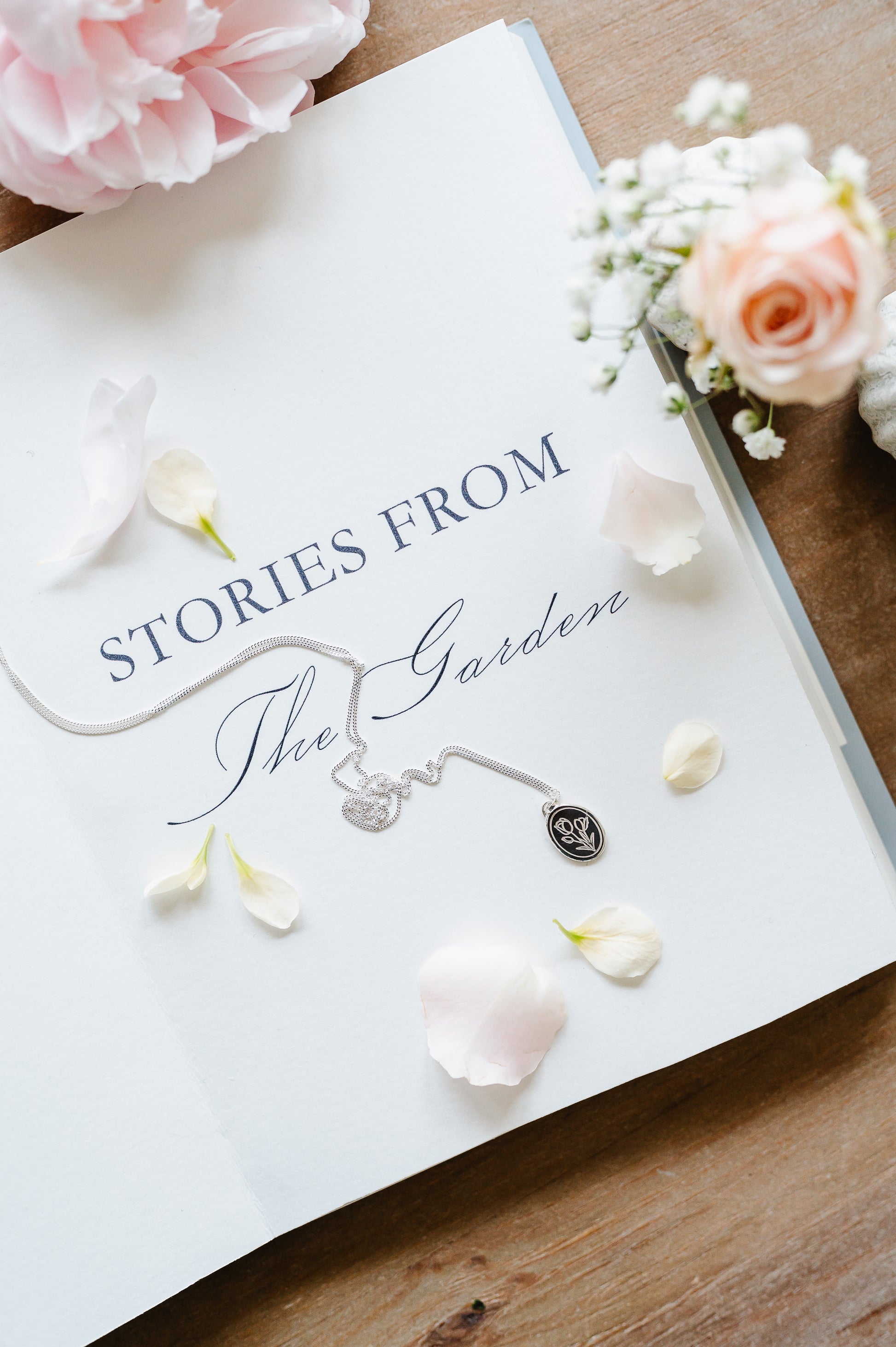 A dainty sterling silver necklace lying on a book with some flowers in the background.