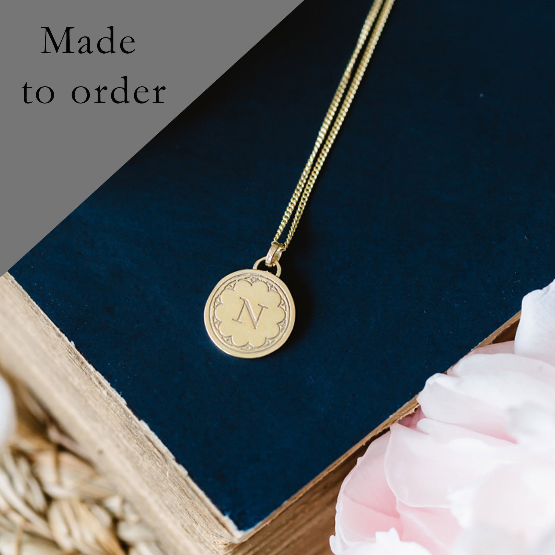 A solid 9ct yellow gold necklace with a round initial pendant, displayed on a book with a part of a golden chain visible.