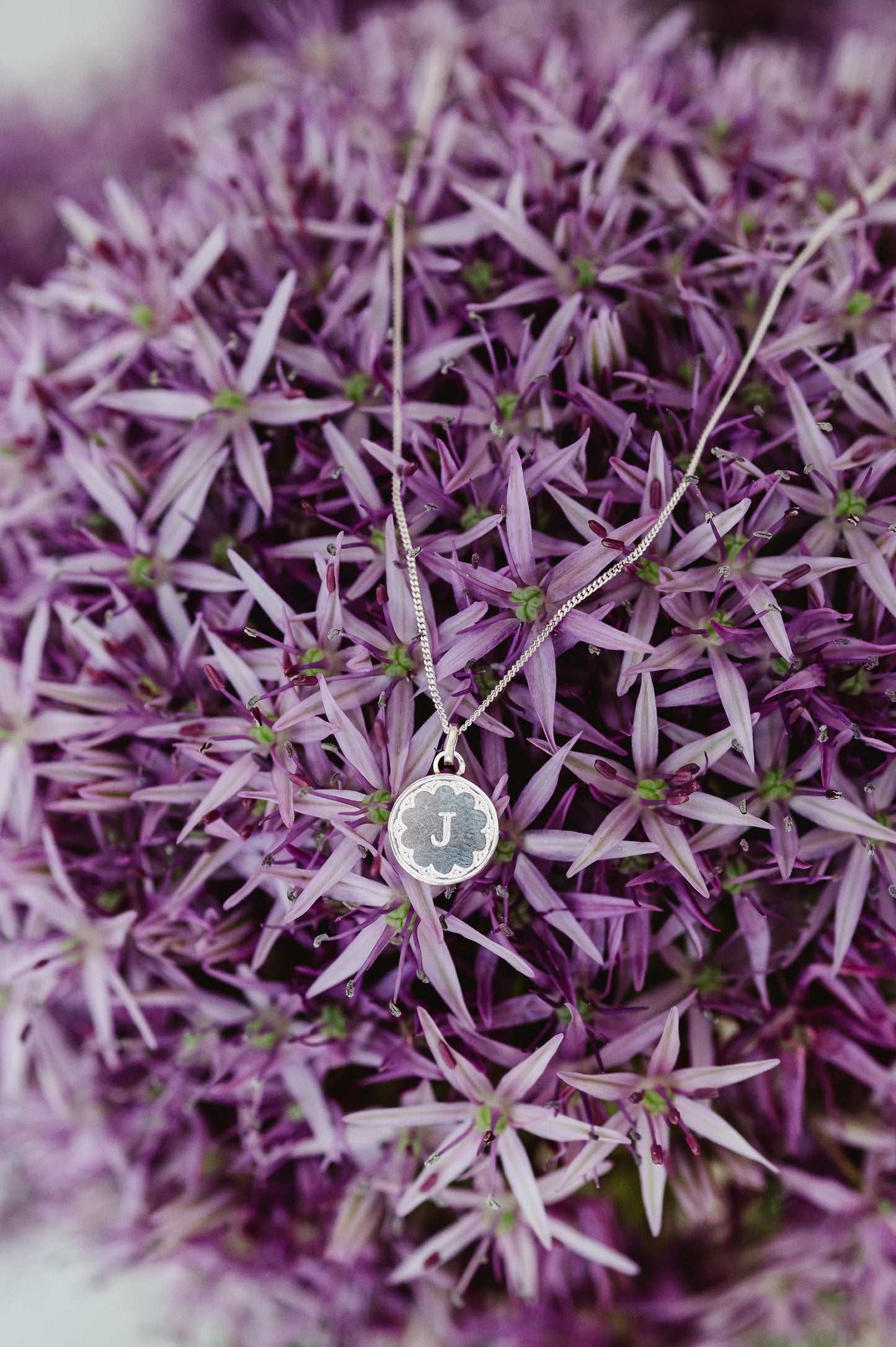 A round initial necklace in sterling silver siting on an allium flower.