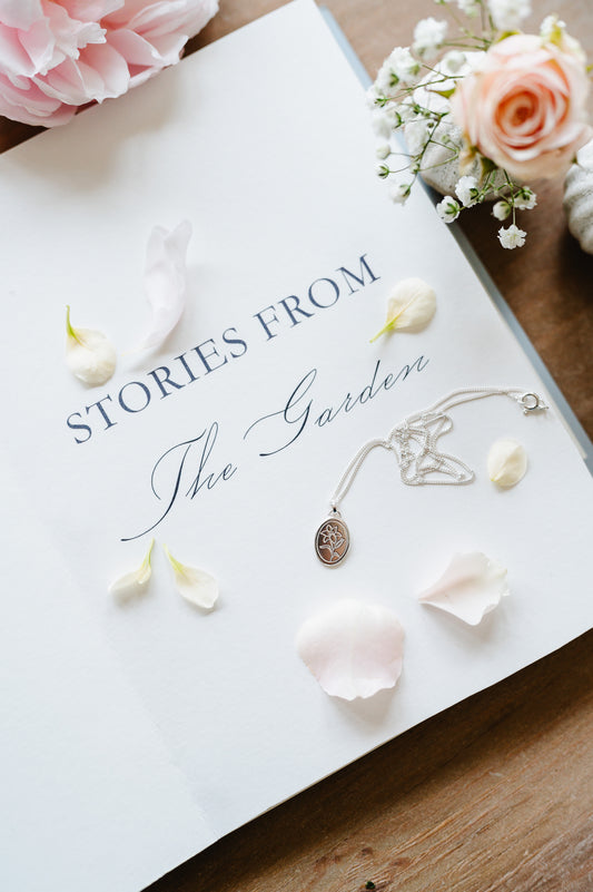 A sterling silver necklace with an oval coin design featuring a lily flower, displayed on a book with flowers.