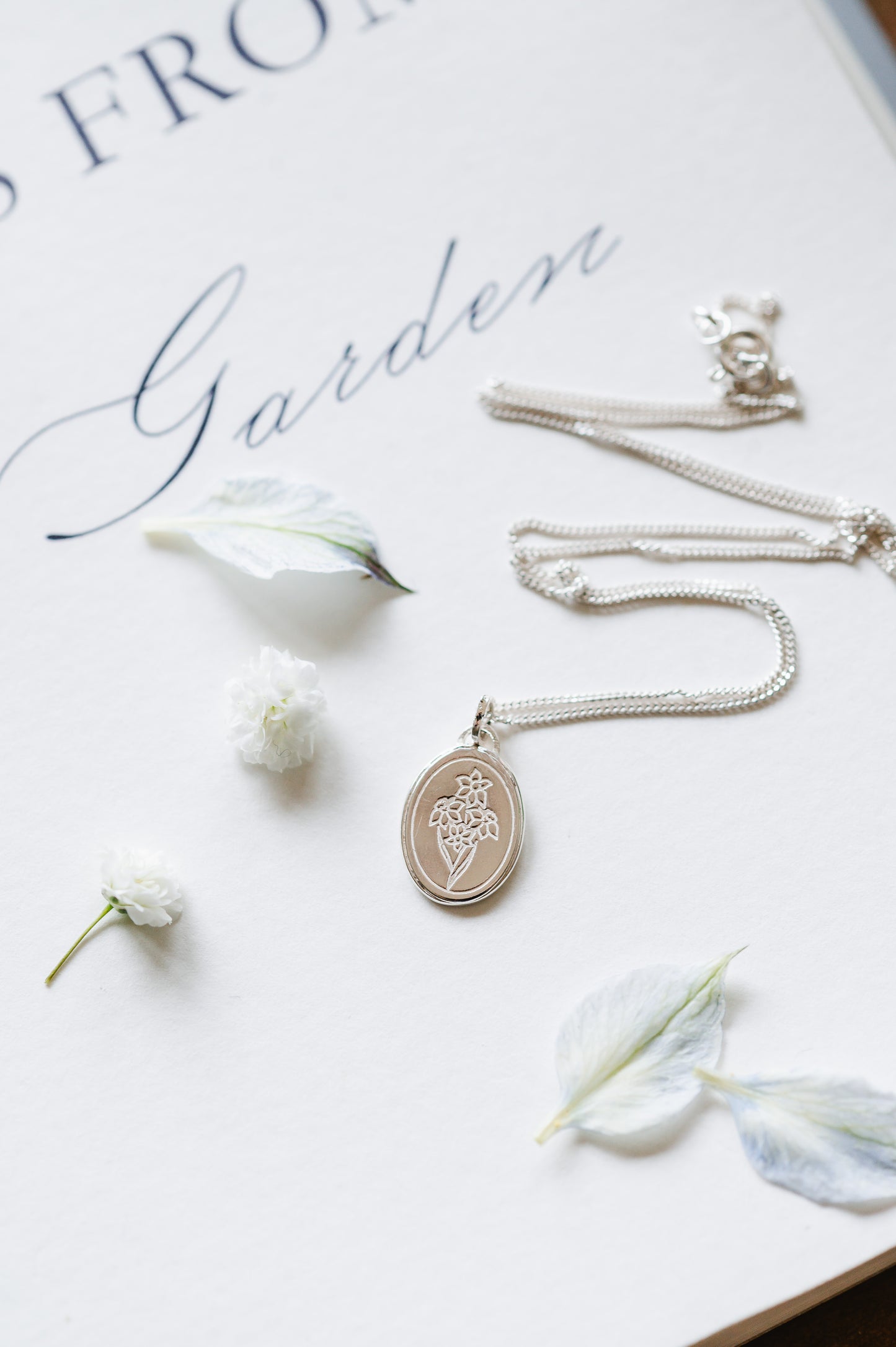 A flower necklace with a narcissus in sterling silver. The dainty necklace is lying on a book page with some petals.