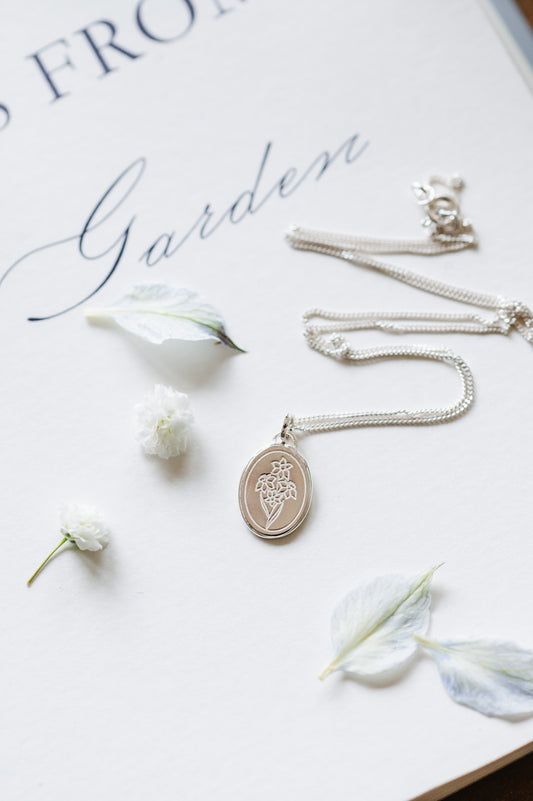 A flower necklace with a narcissus in sterling silver. The dainty necklace is lying on a book page with some petals.
