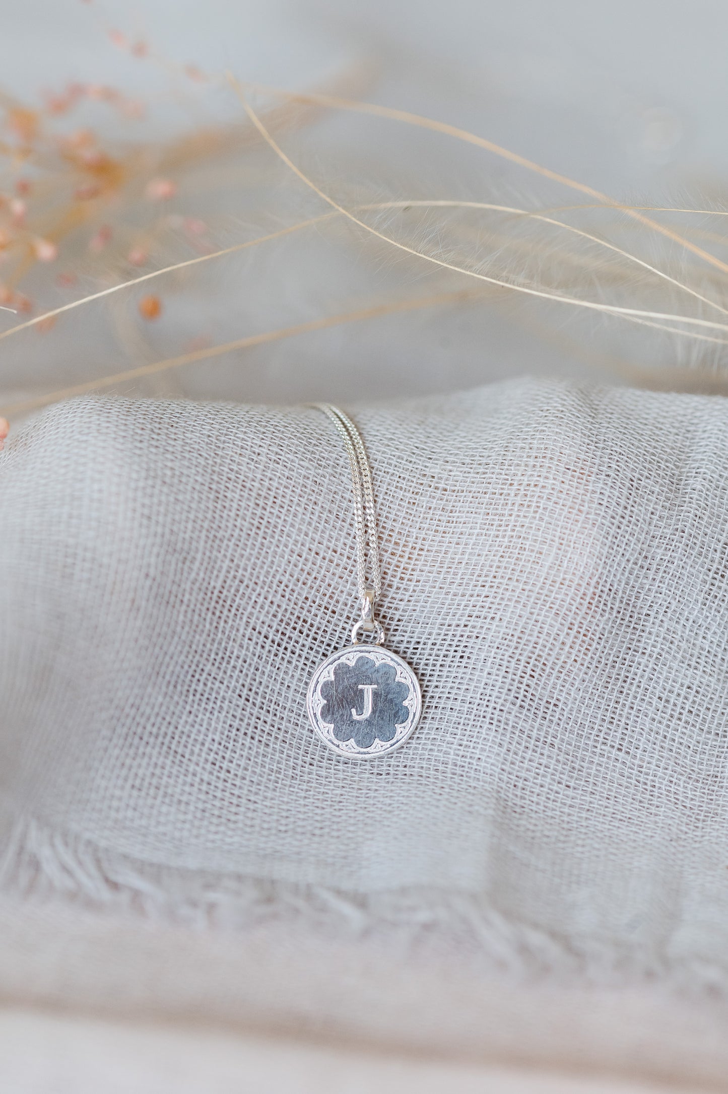 A sterling silver initial necklace sitting on pale blue linen