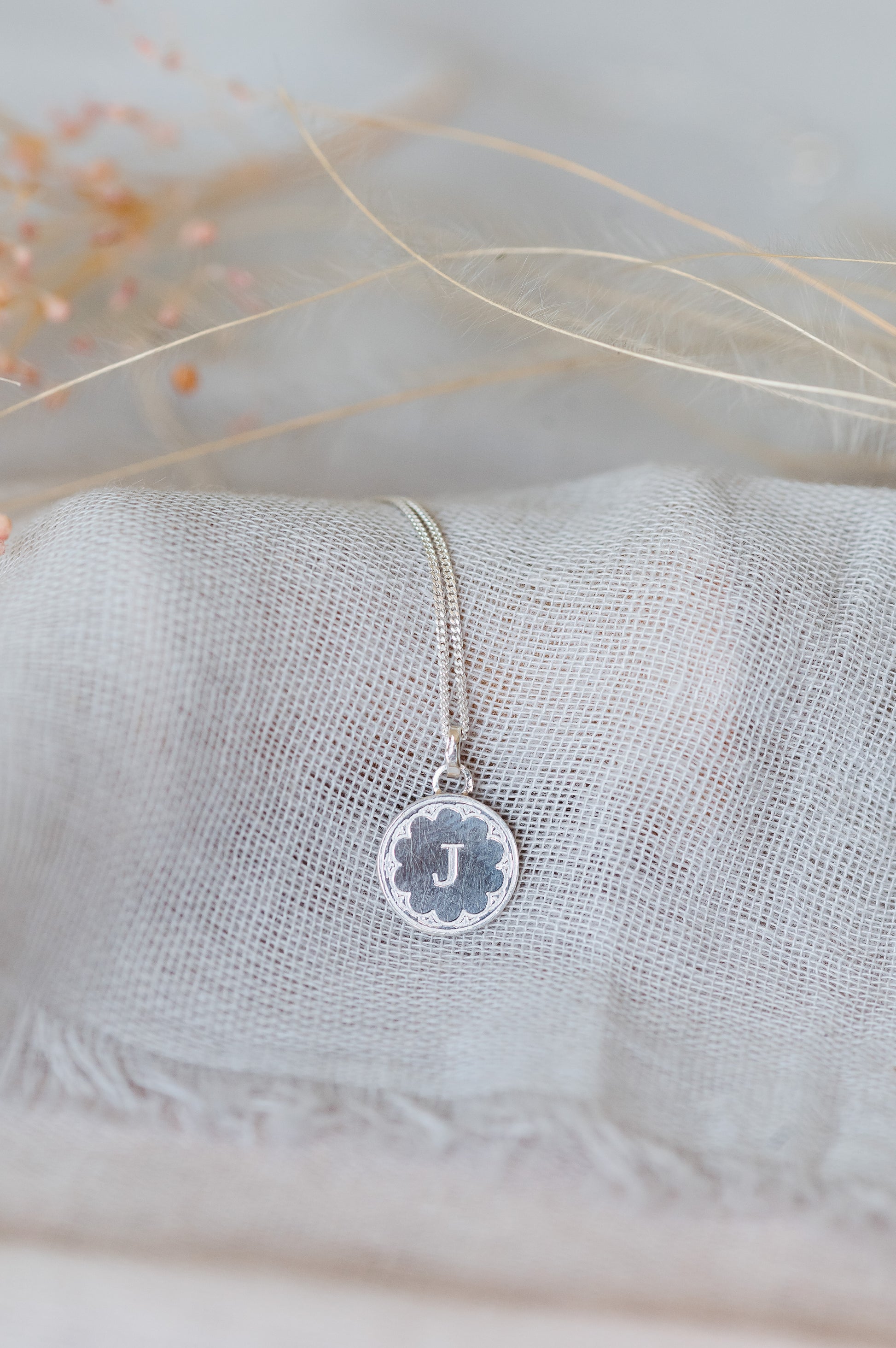 A sterling silver initial necklace sitting on pale blue linen