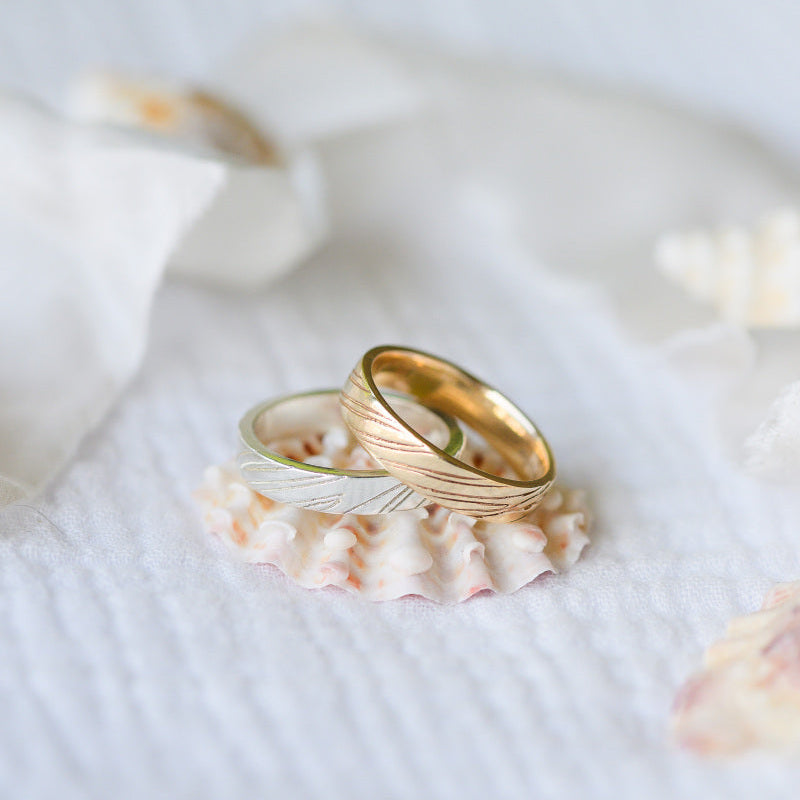Two wedding rings, one gold one silver stacked on a seashell, sand rings.