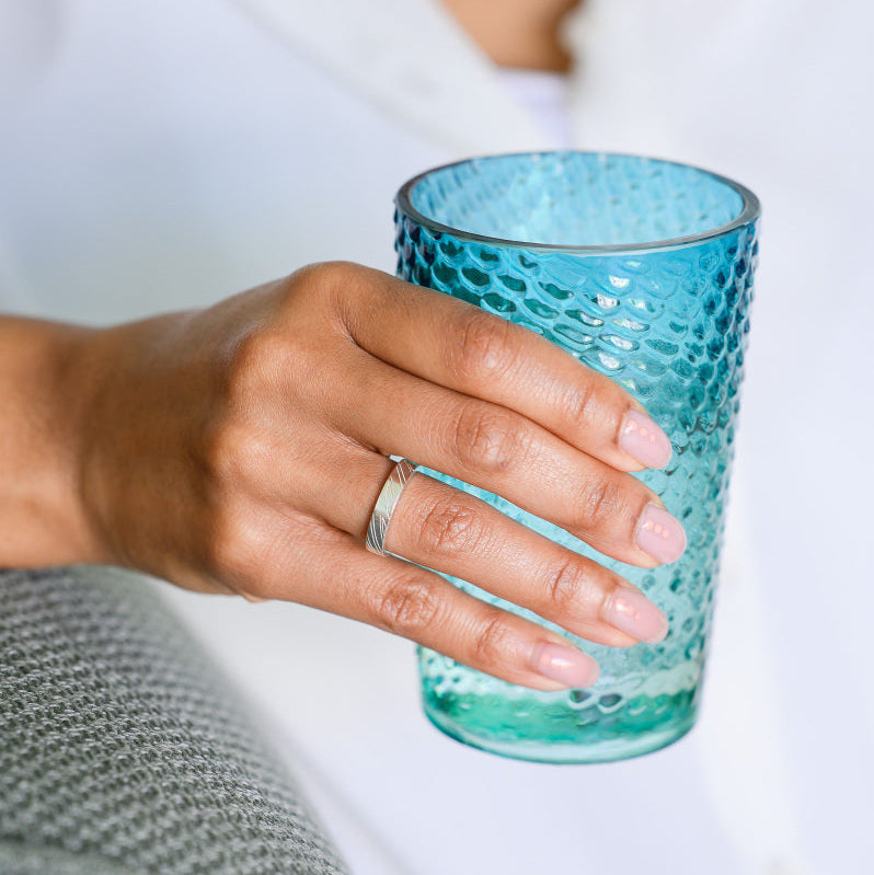Hand holding a glass, wearing a sterling silver wedding ring with carved detail