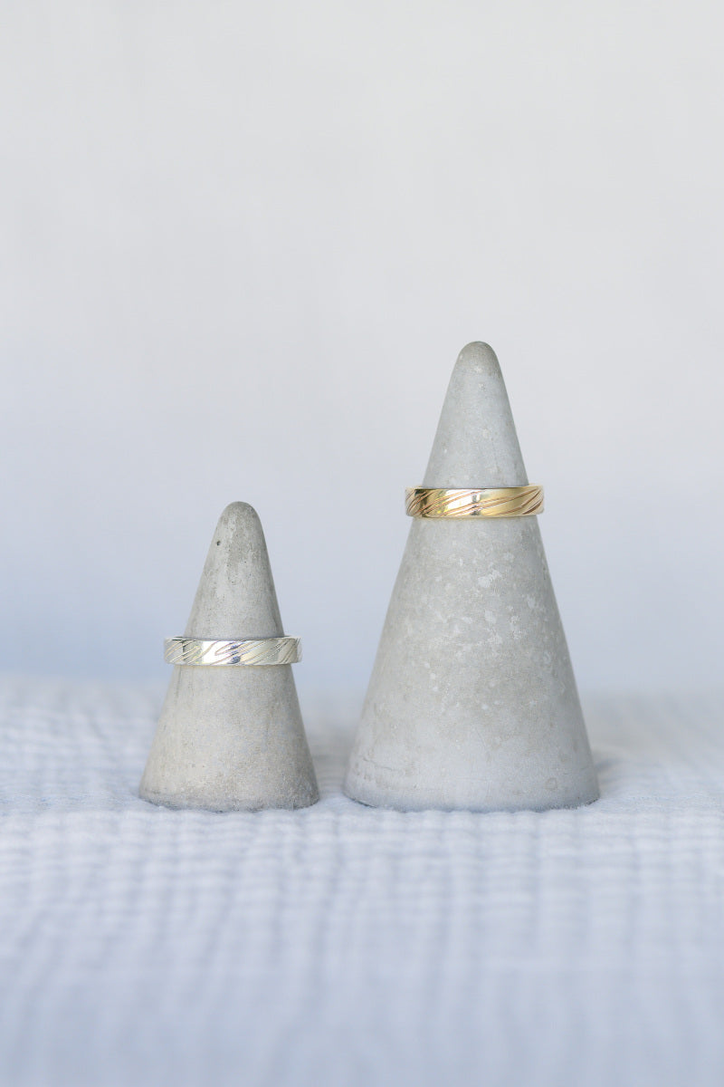 Two wedding rings with grooved details on concrete ring stands.